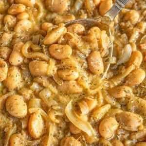 French onion butter beans in a skillet with a silver spoon and bright daylight.