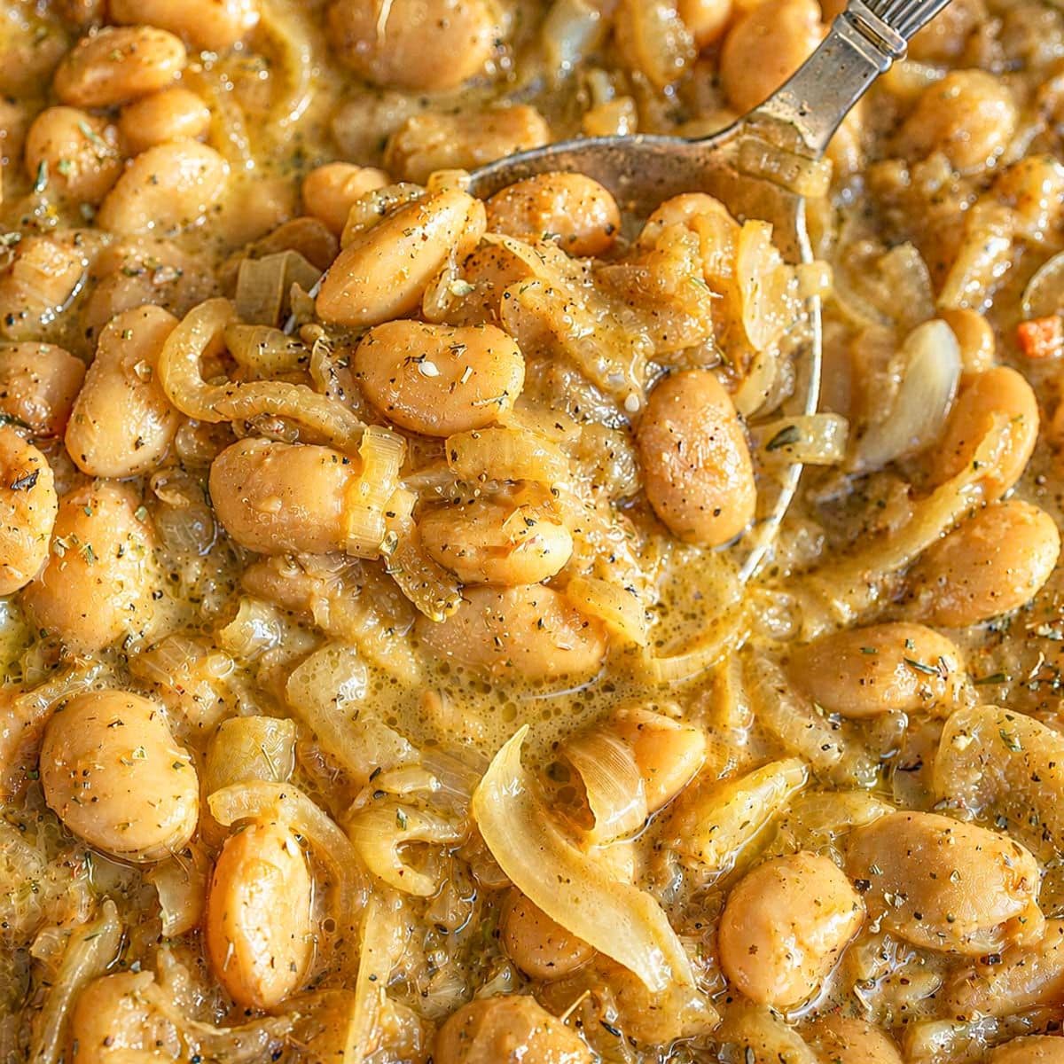French onion butter beans in a skillet with a silver spoon and bright daylight.