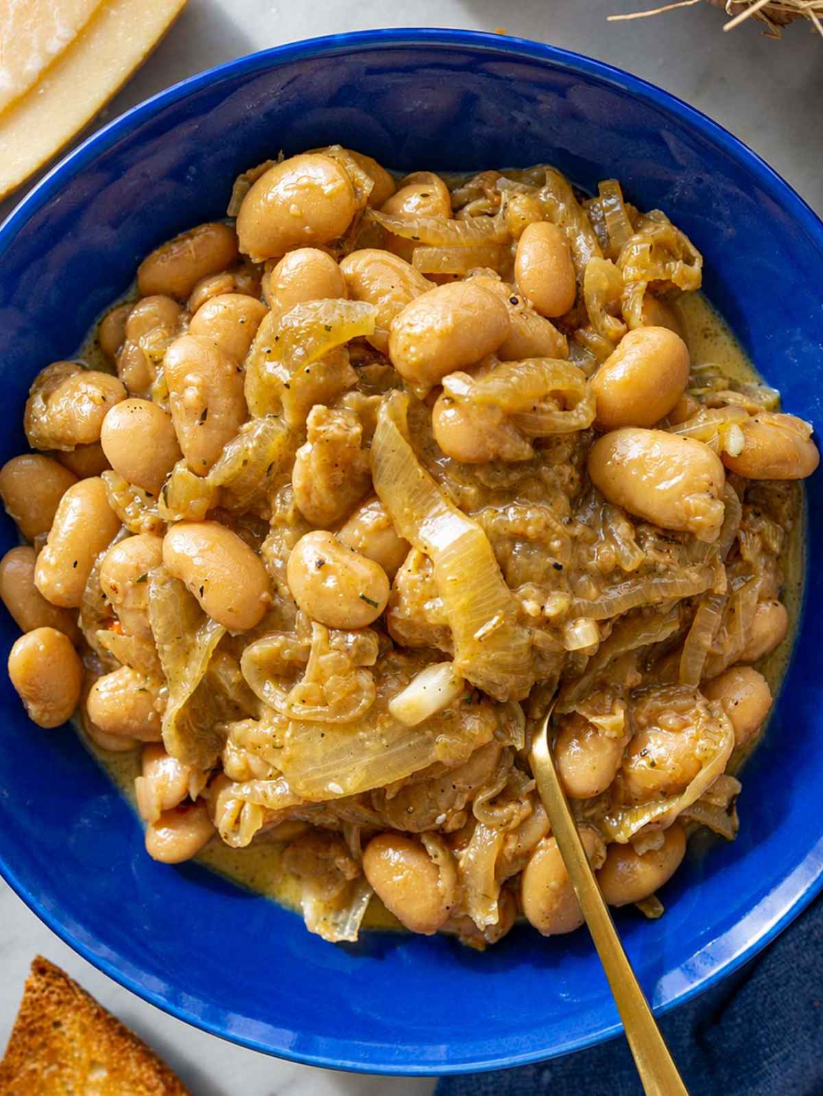 French onion butter beans in blue bowl with caramelized onions and Parmesan.