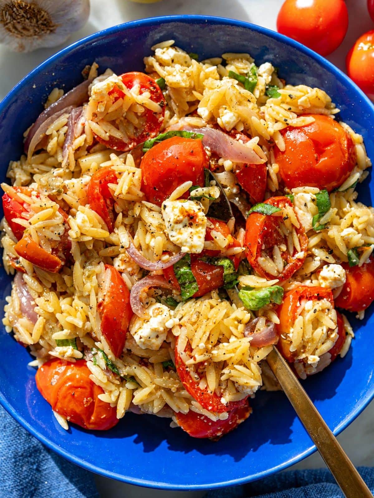 Glossy roasted tomato orzo in a bowl with creamy feta and fresh basil.