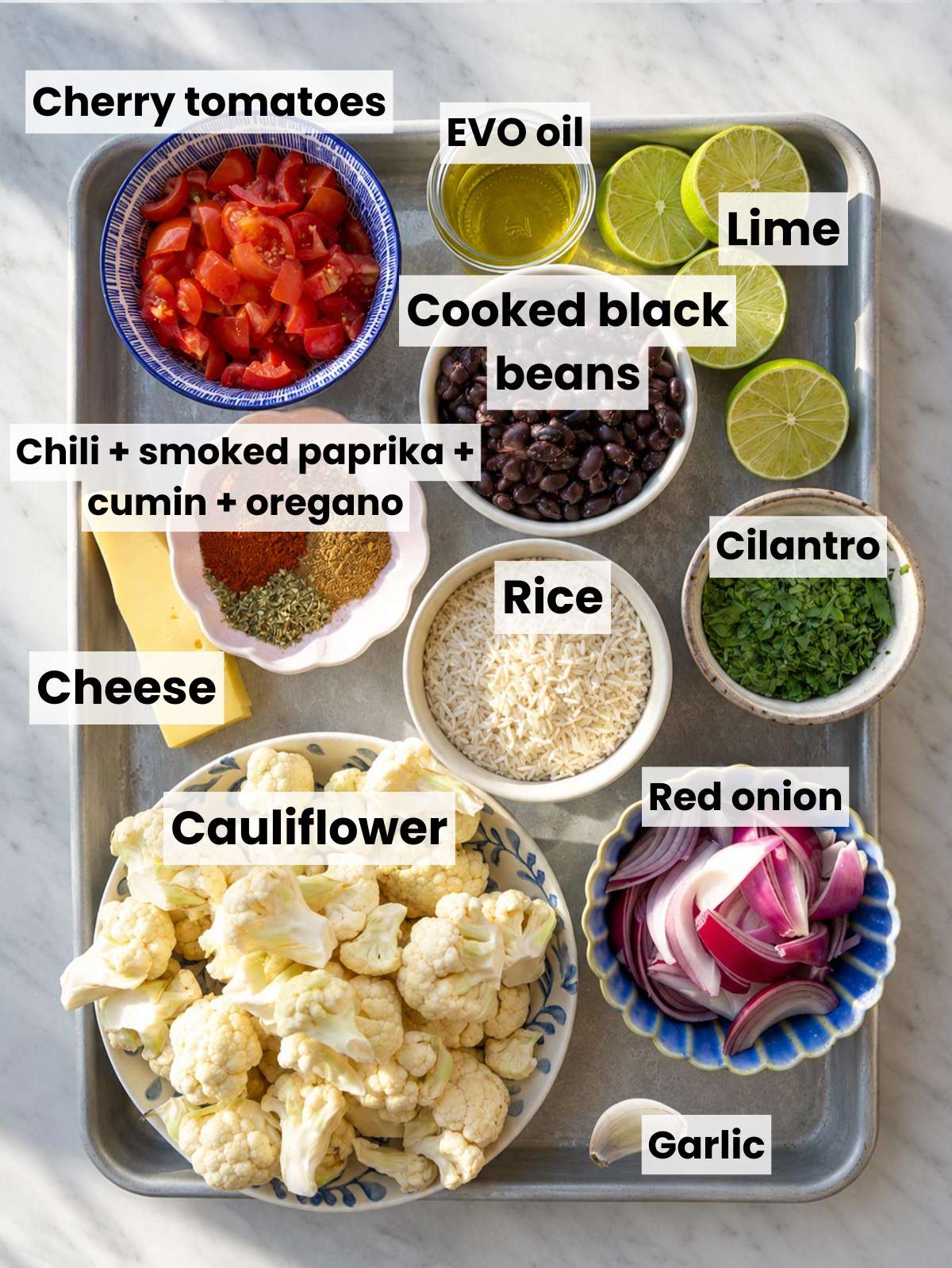Ingredients for Cauliflower Burrito Bowl arranged on white marble with spices and herbs.