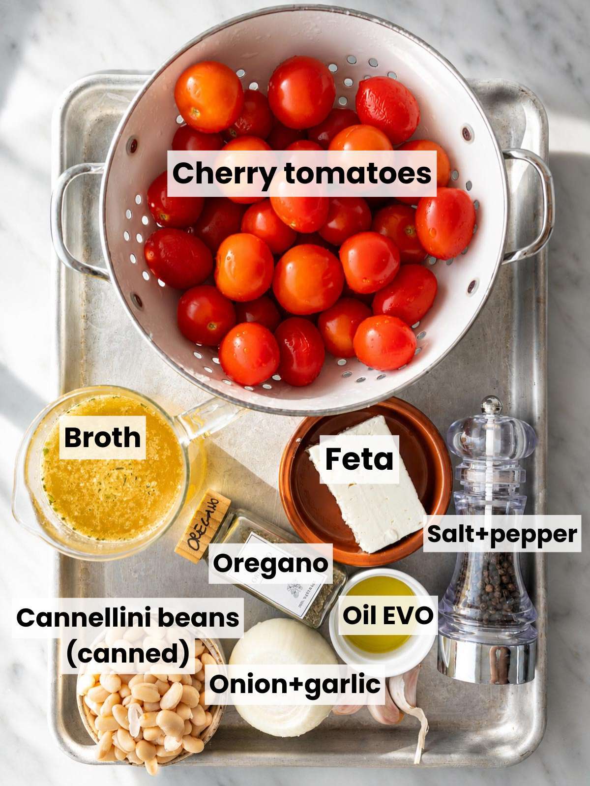 Ingredients for roasted tomato soup on white marble countertop.
