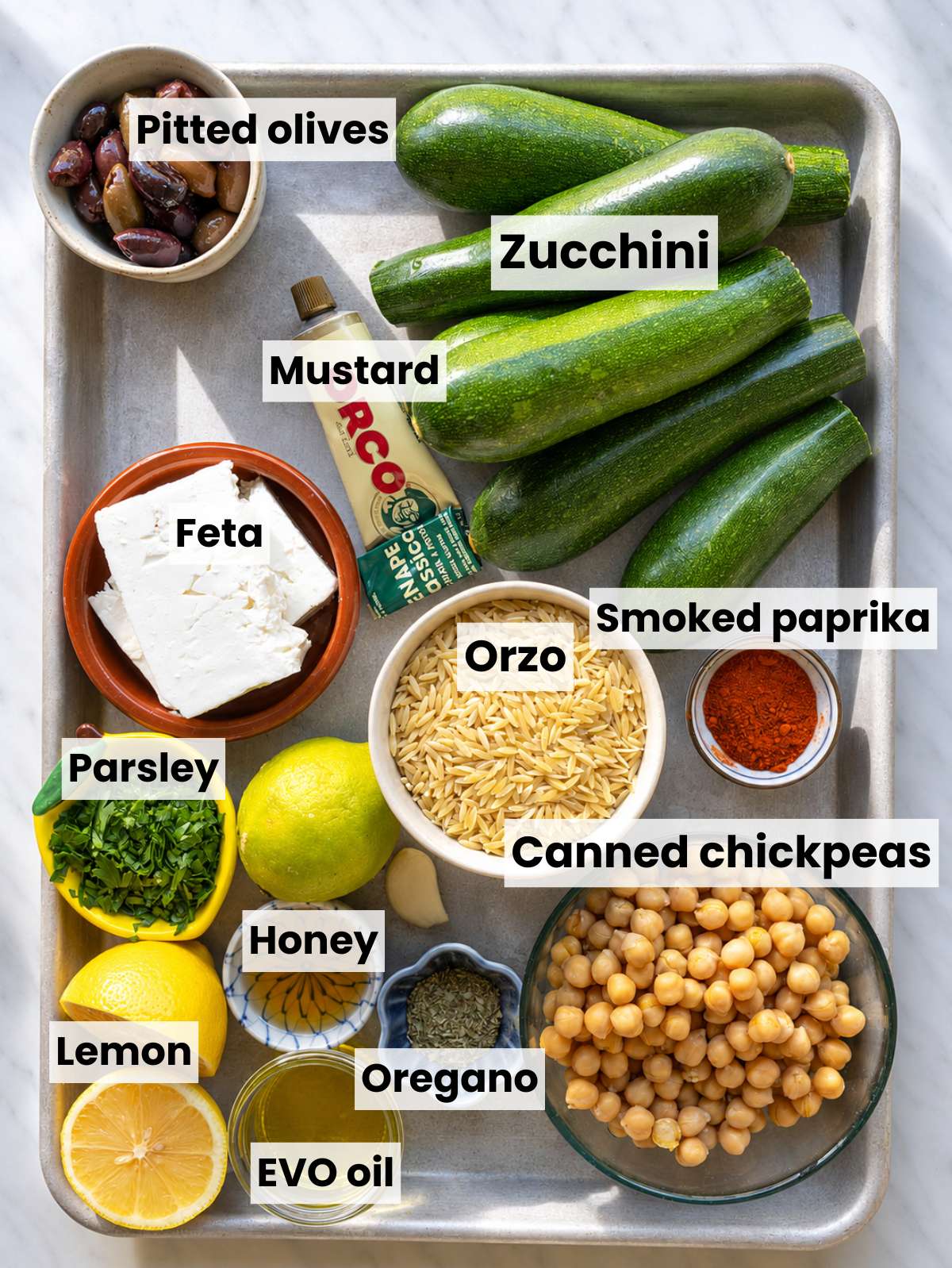 Ingredients for roasted zucchini orzo arranged on white marble in natural daylight.