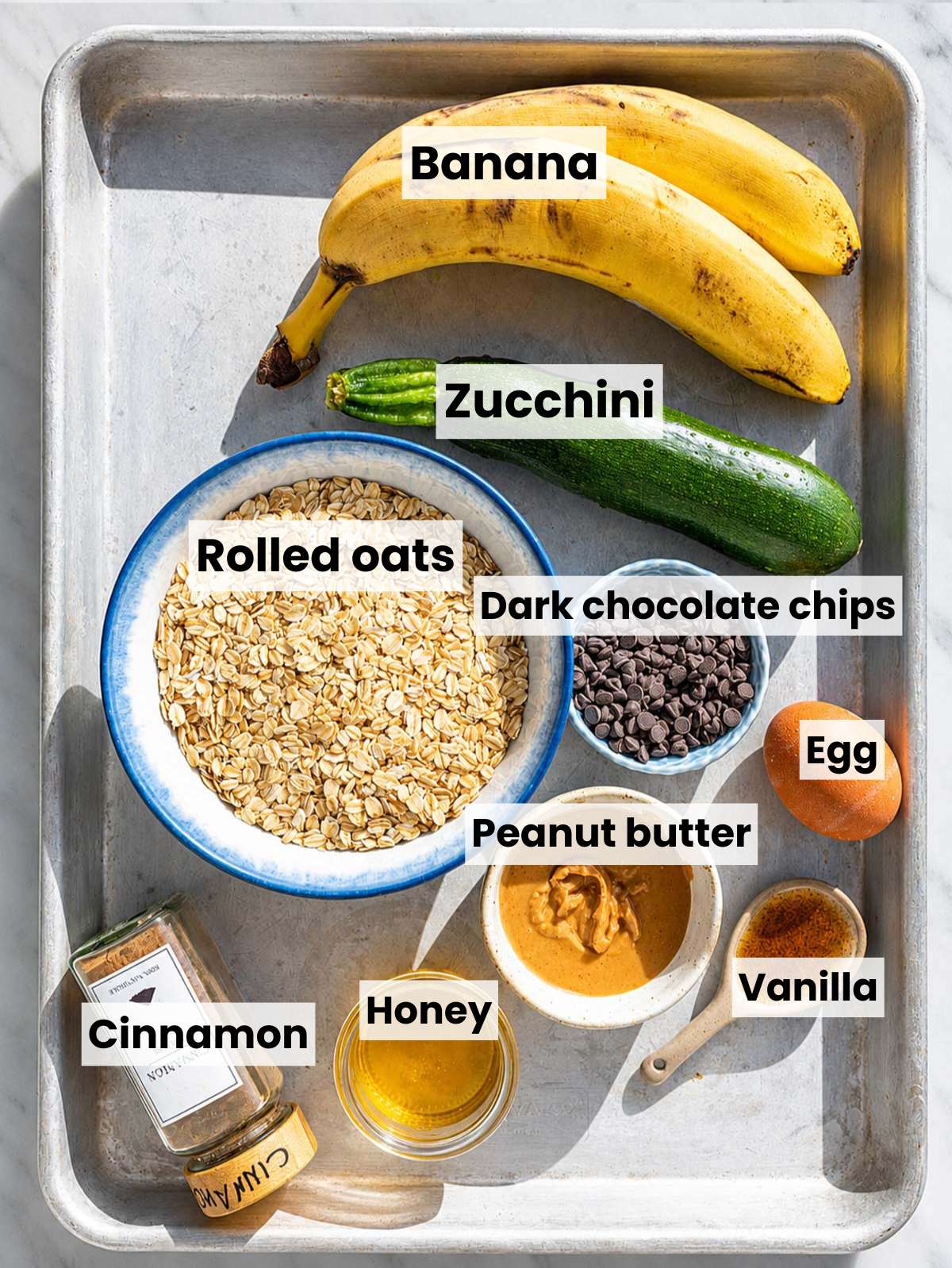 Ingredients for zucchini banana bars on white marble in natural window light.