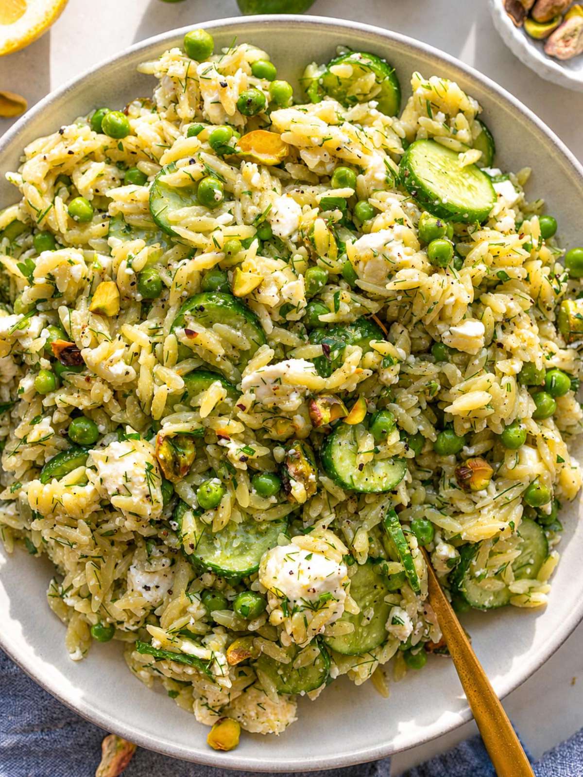 Lemon orzo salad with peas, cucumber, feta, herbs, and pistachios in daylight.