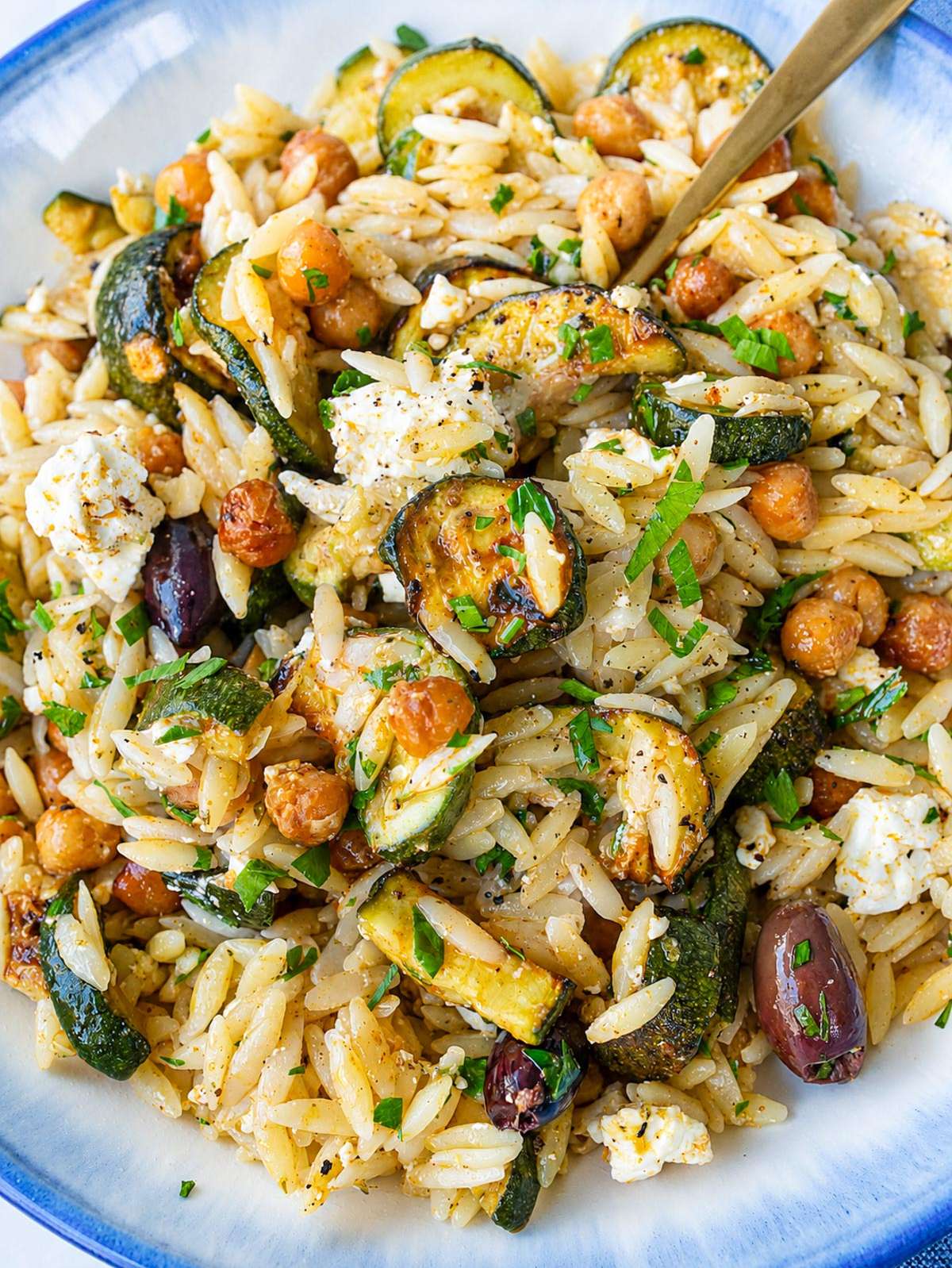 Roasted zucchini orzo with feta, olives, chickpeas, and parsley in serving bowl.
