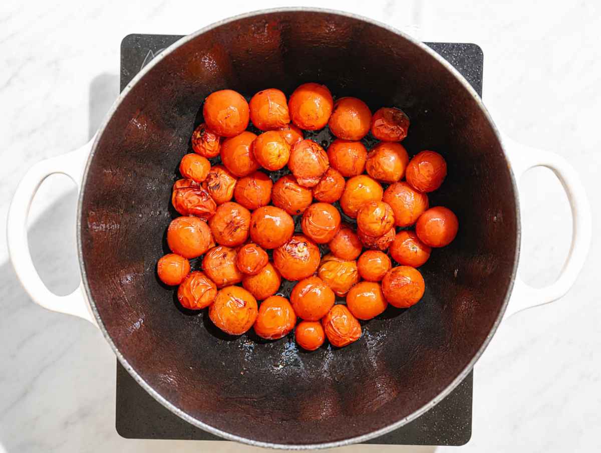 Step 1 Cherry tomatoes bursting in olive oil inside a large pot.