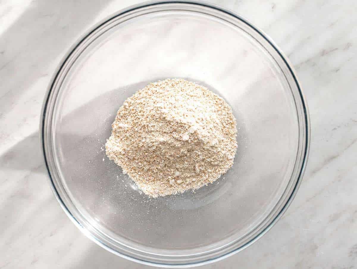 Step 1 Rolled oats blending into fine oat flour in a food processor on marble countertop.