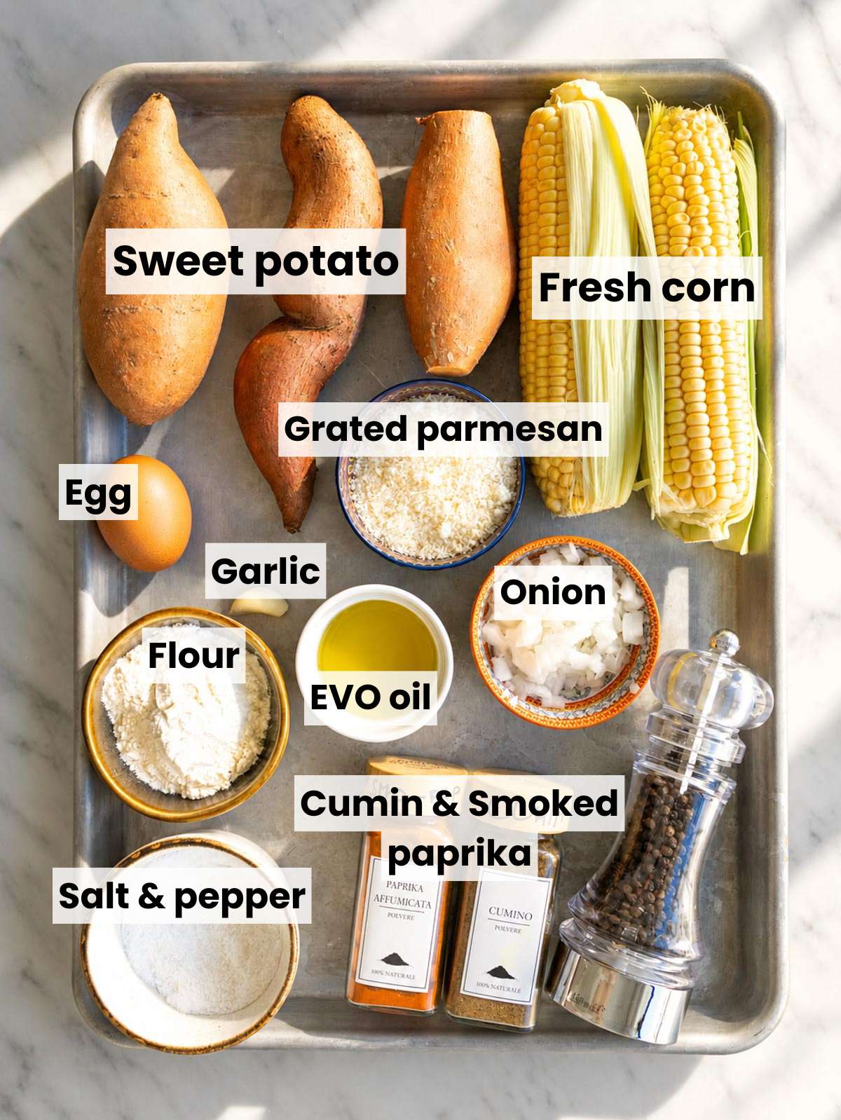 Sweet potatoes, corn, Parmesan, egg, spices, and flour on white marble.