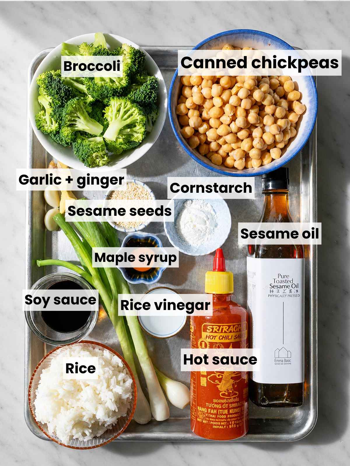 Broccoli, chickpeas, aromatics, and sauce ingredients arranged on marble.