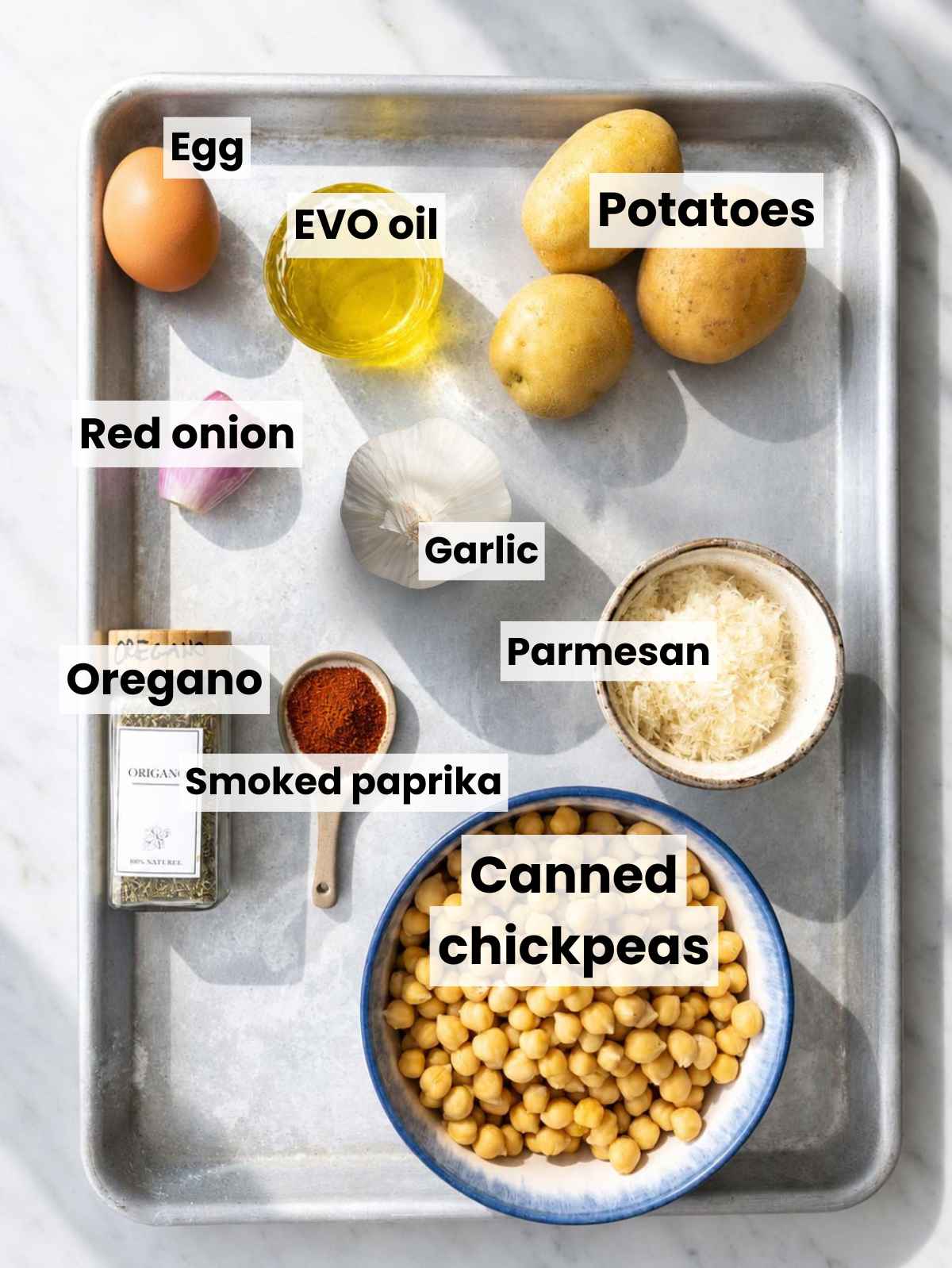 Canned chickpeas, potatoes, Parmesan, egg, onion, garlic, spices, and olive oil on marble.