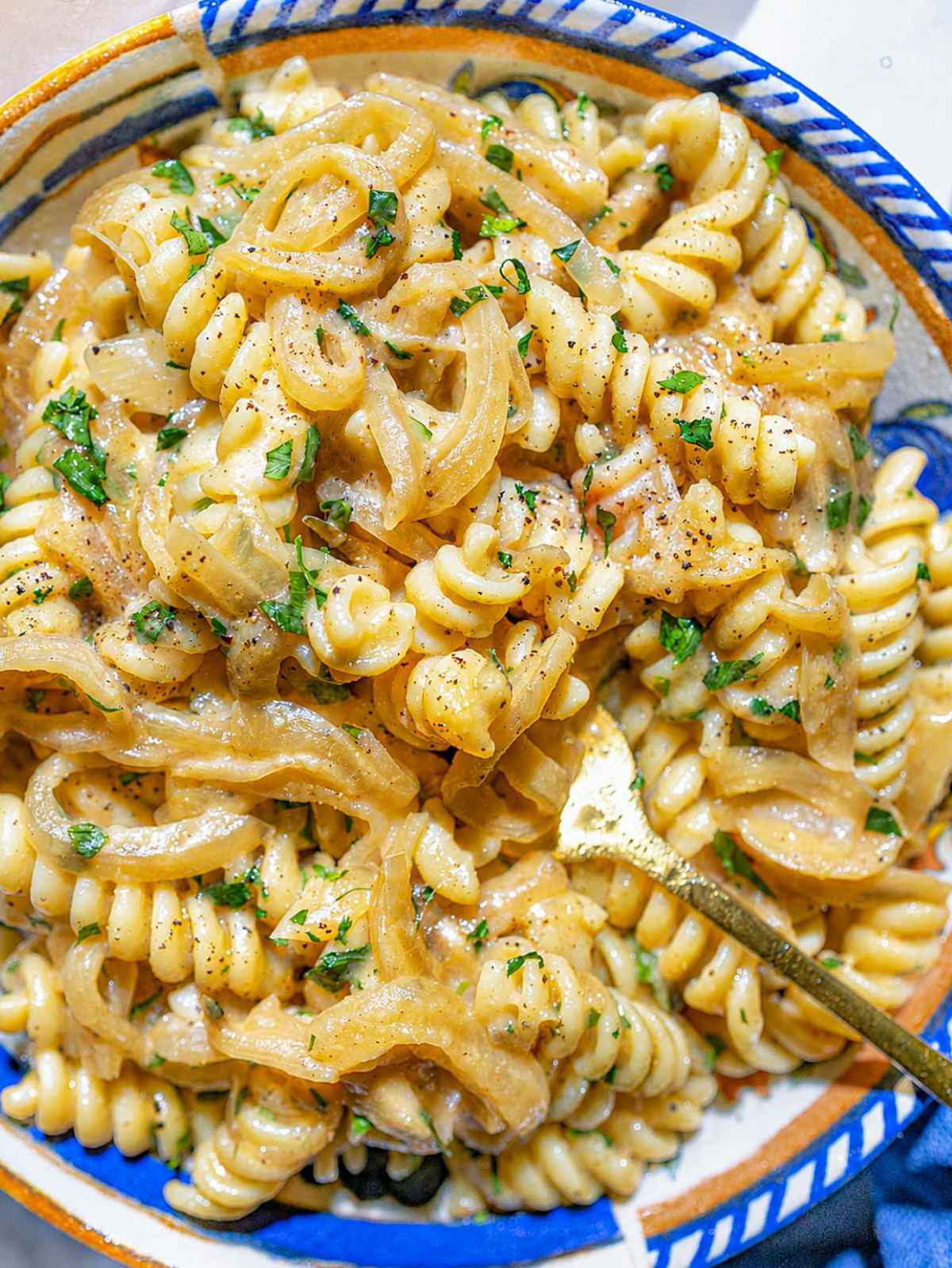 Close-up of creamy fusilli coated with hummus sauce and caramelized onions.