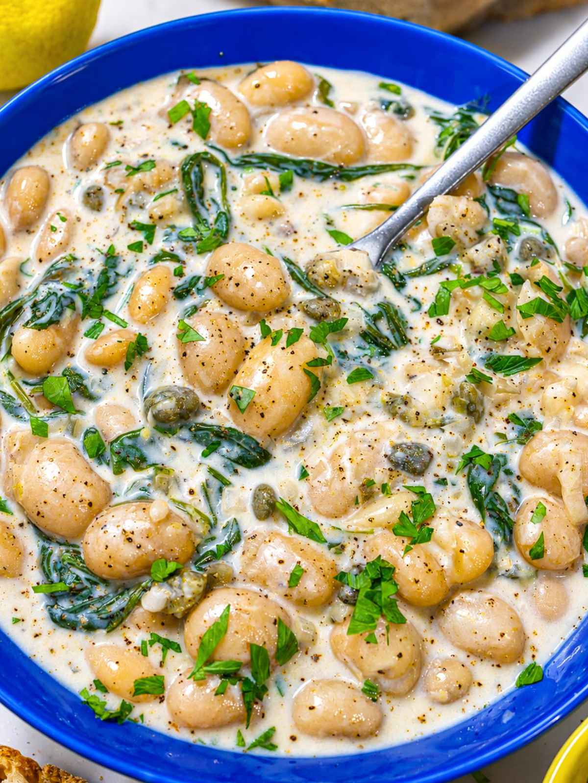 Close-up of glossy butter beans coated in creamy lemon caper sauce in a bowl.