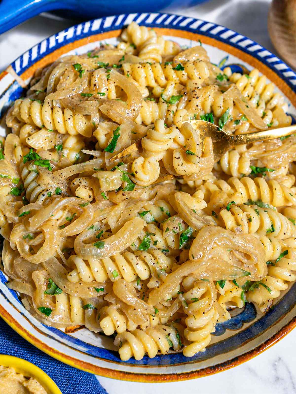 Close-up of glossy fusilli coated with creamy sauce and caramelized onions.
