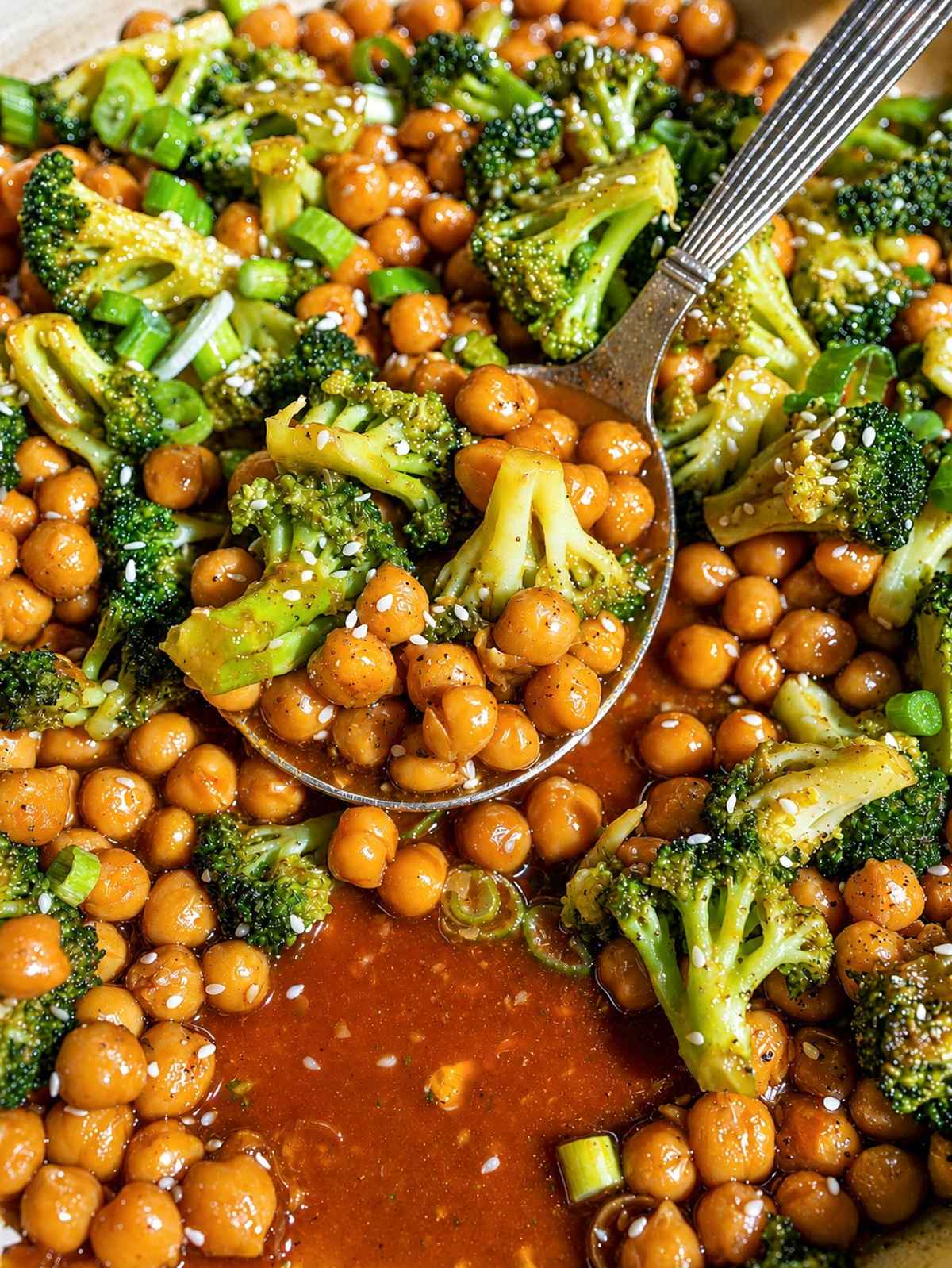 Close-up of glossy sesame chickpeas with charred broccoli and scallions.