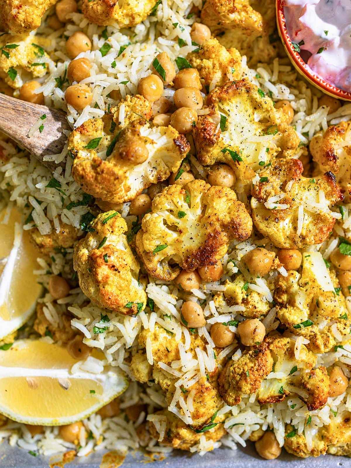 Close-up of glossy tandoori cauliflower, chickpeas, basmati rice, cilantro, and raita.