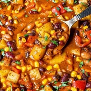 Cowboy Bean Soup with spoon lifting three beans, potatoes, corn, and tomato broth.
