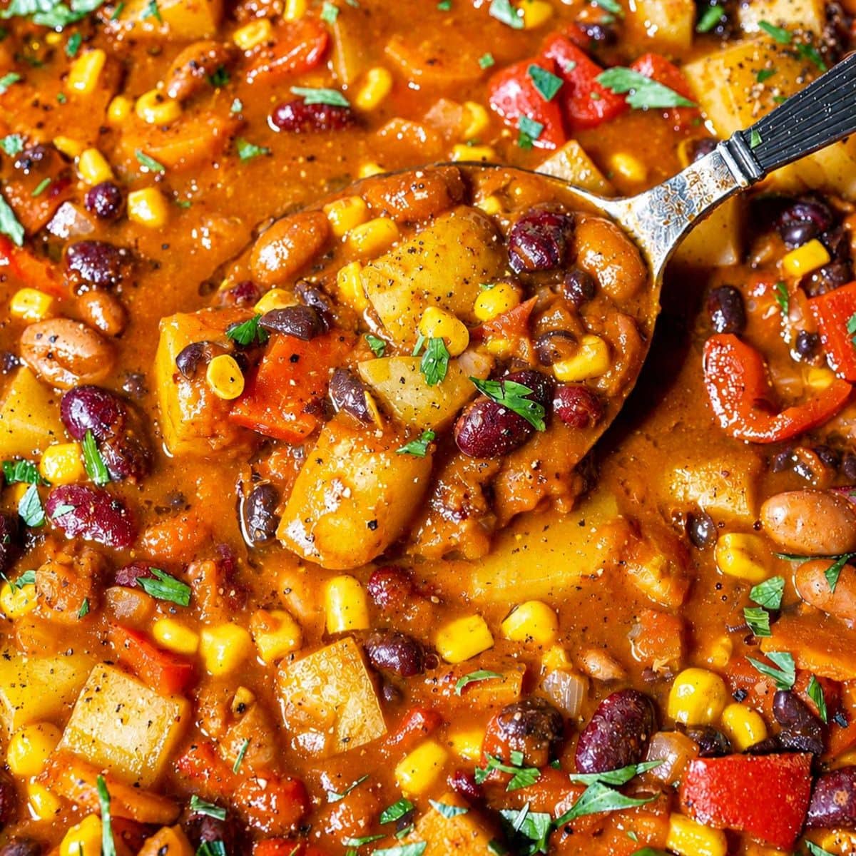 Cowboy Bean Soup with spoon lifting three beans, potatoes, corn, and tomato broth.