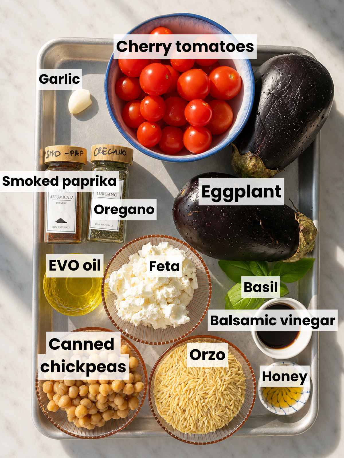 Eggplant, tomatoes, chickpeas, orzo, feta, herbs, and seasonings on marble.