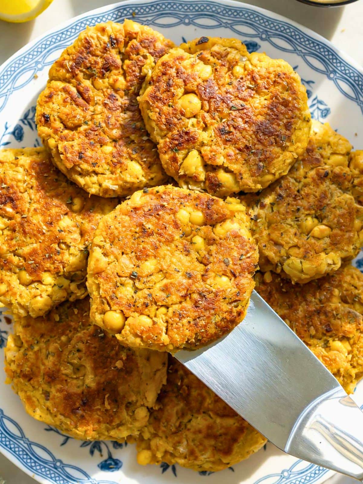 Golden chickpea potato patties stacked served with spatula and oregano.