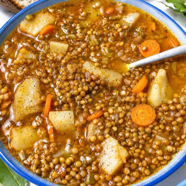 Hearty French lentil soup with crushed pepper and crusty bread on marble.
