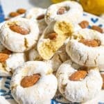 Lemon Almond Cookies piled on marble with crackled powdered sugar and whole almonds.