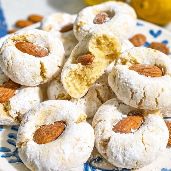 Lemon Almond Cookies piled on marble with crackled powdered sugar and whole almonds.