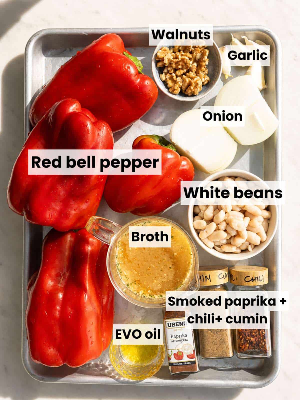 Red peppers, onion, garlic, beans, walnuts, spices, and olive oil on marble.