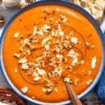 Roasted red pepper soup with walnuts, feta, and olive oil and a spoon.