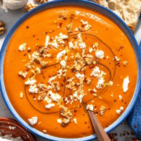 Roasted red pepper soup with walnuts, feta, and olive oil and a spoon.