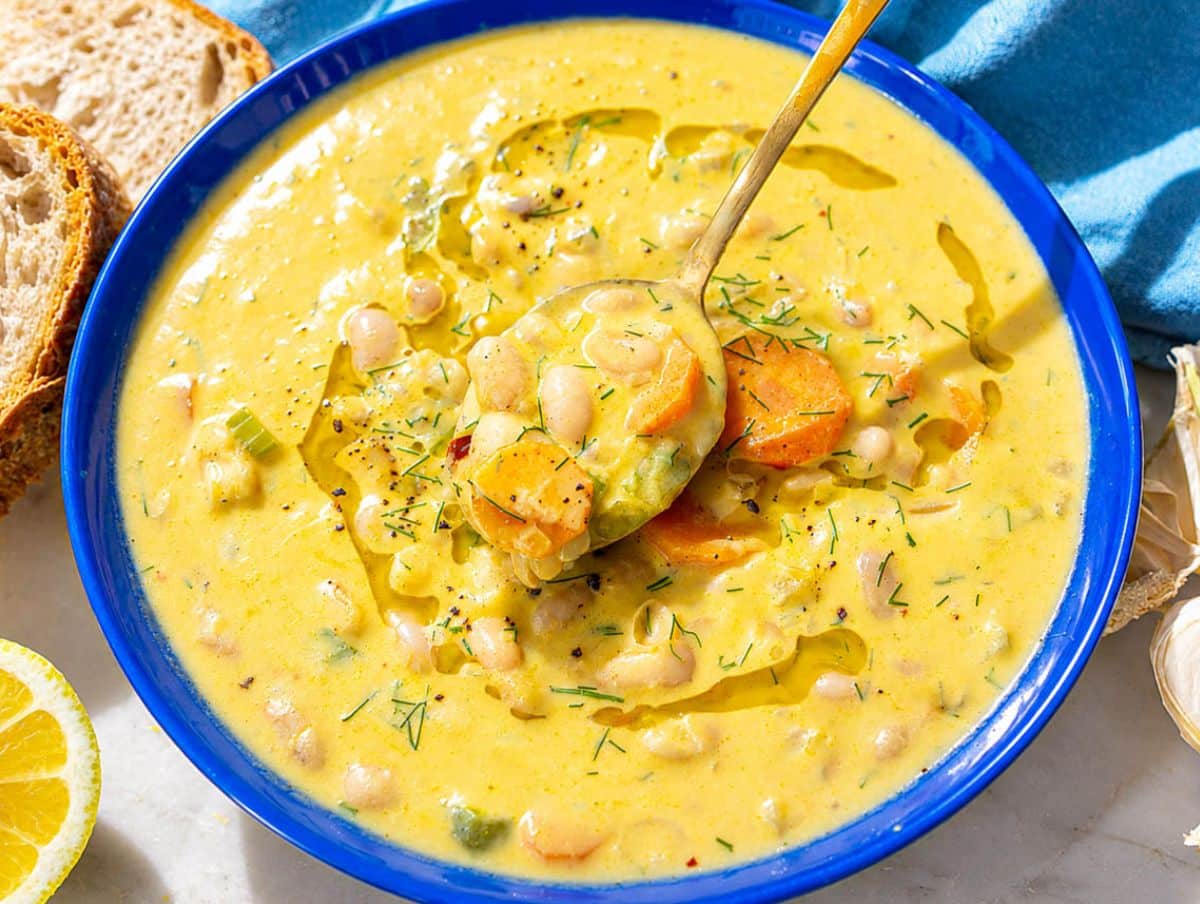 Spoon lifting creamy Lemon White Bean Soup with beans, carrots, and fresh dill.