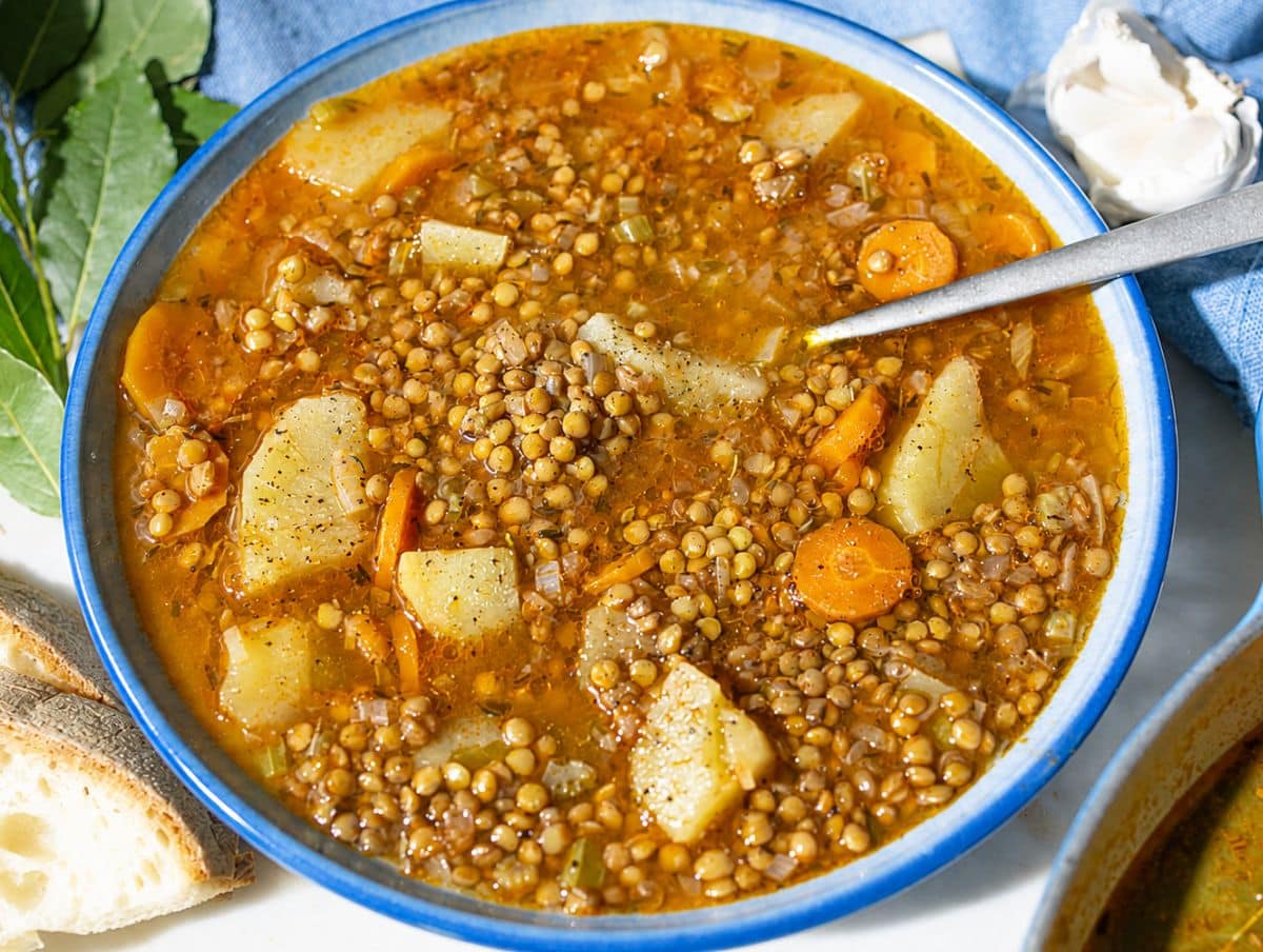 Steaming French lentil soup with rustic vegetables and bread in natural light.