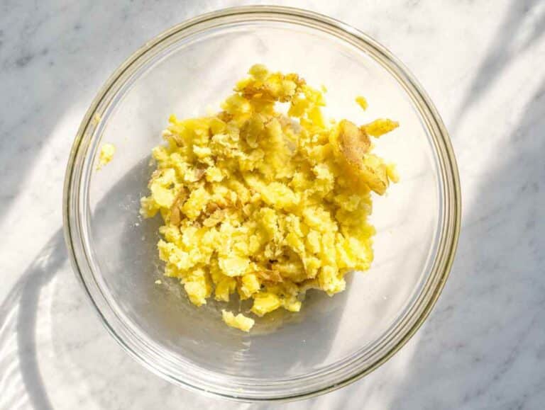 Step 1 Cooked skin-on potatoes being mashed in a bowl until soft and chunky.
