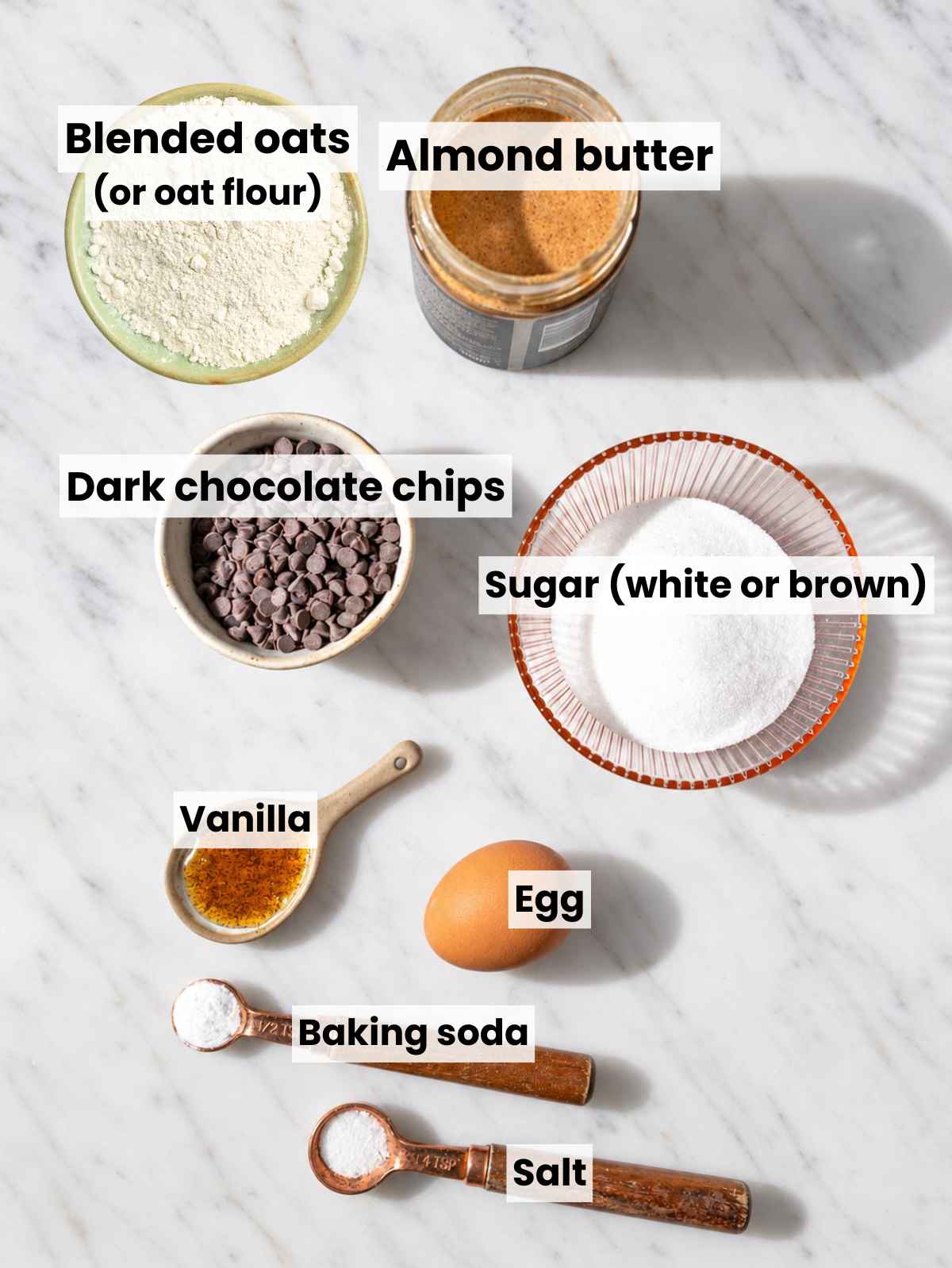 Almond butter chocolate chip cookie ingredients arranged on marble in natural light