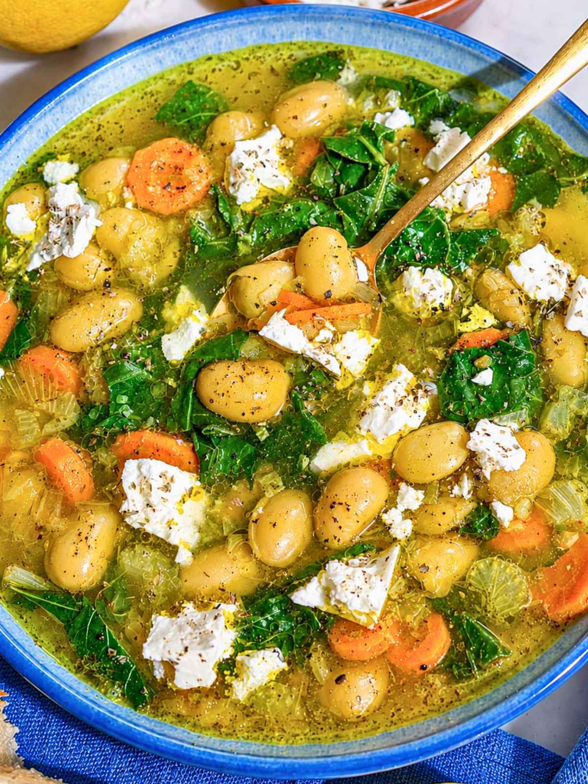 Close-up of glossy butter beans, spinach, feta, and golden broth
