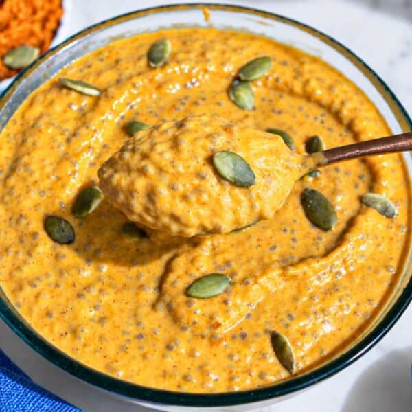 Creamy pumpkin chia pudding with seeds and a lifted golden spoon.