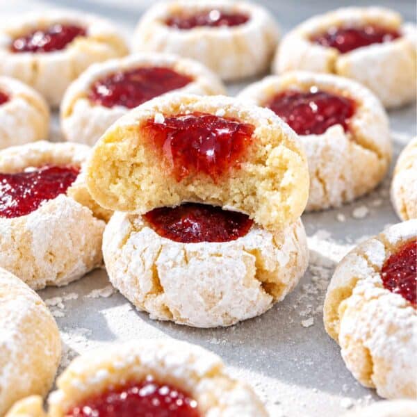 A bitten almond flour thumbprint cookie showing its soft golden crumb and jam filling, resting on another cookie.