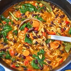 A pot of black bean orzo soup with vegetables and spinach.