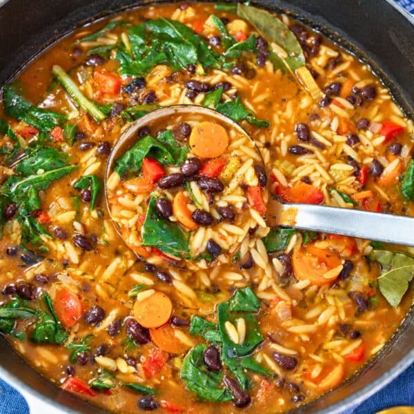 A pot of black bean orzo soup with vegetables and spinach.