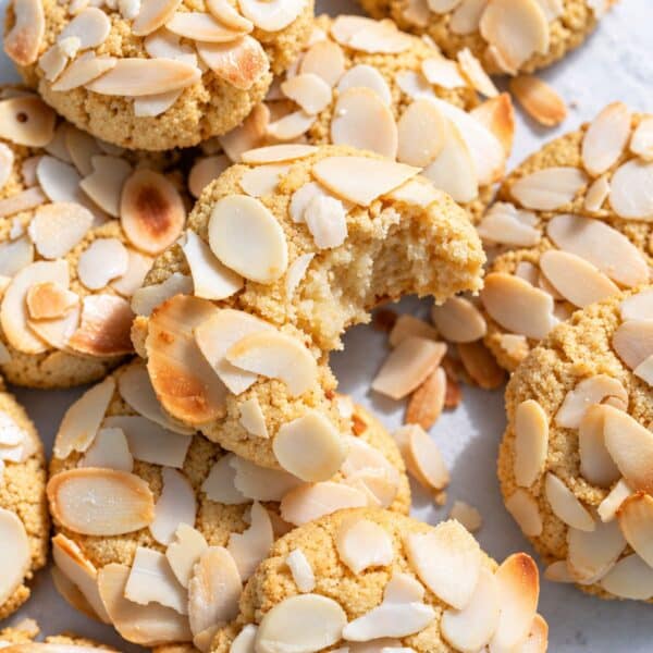 Almond croissant cookies with a bite piled together with toasted almonds.