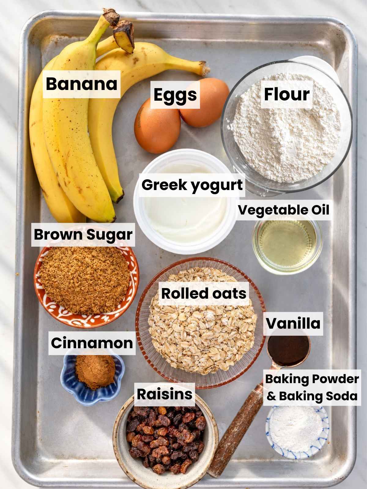 Bananas, oats, raisins, Greek yogurt, and other muffin ingredients on marble.