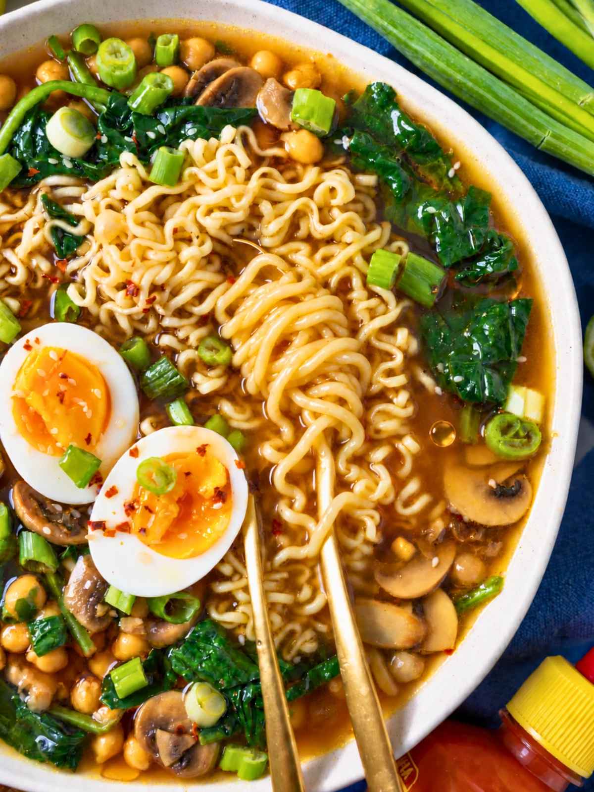 Close-up of ramen noodles, chickpeas, mushrooms, and egg in golden broth.