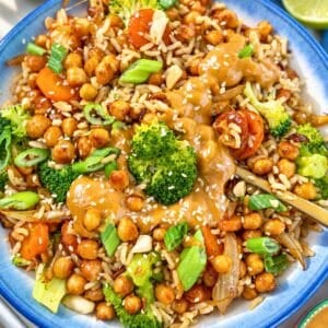 Colorful chickpea rice bowl topped with peanut sauce and chopped scallions.