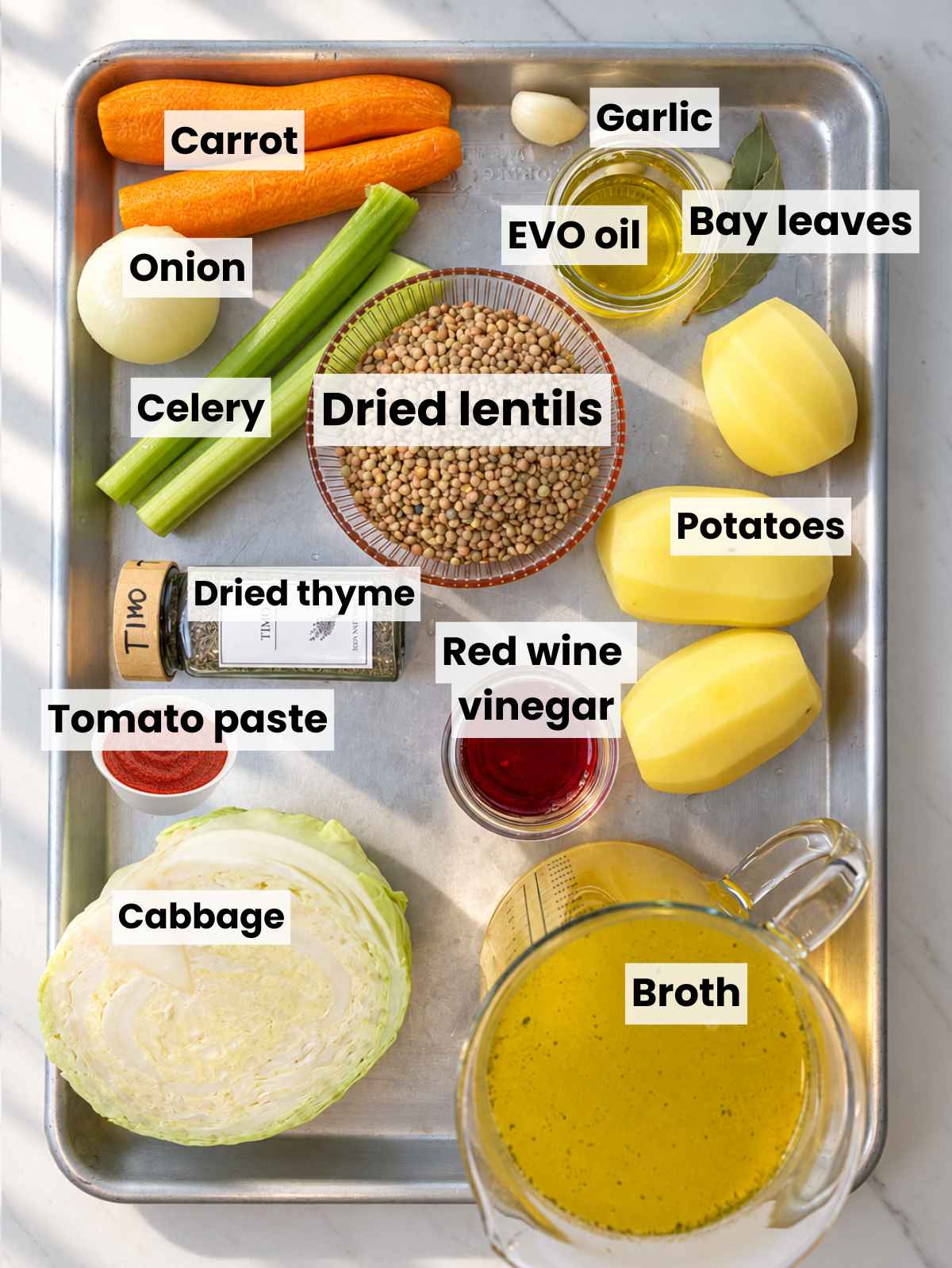 Fresh cabbage, potatoes, carrots, lentils, and soup ingredients arranged on marble.
