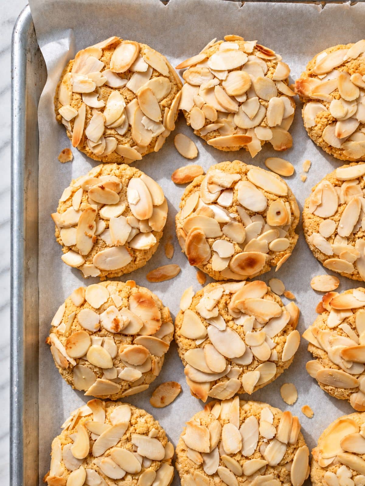 Golden almond croissant cookies topped with split almonds on baking paper and tray.