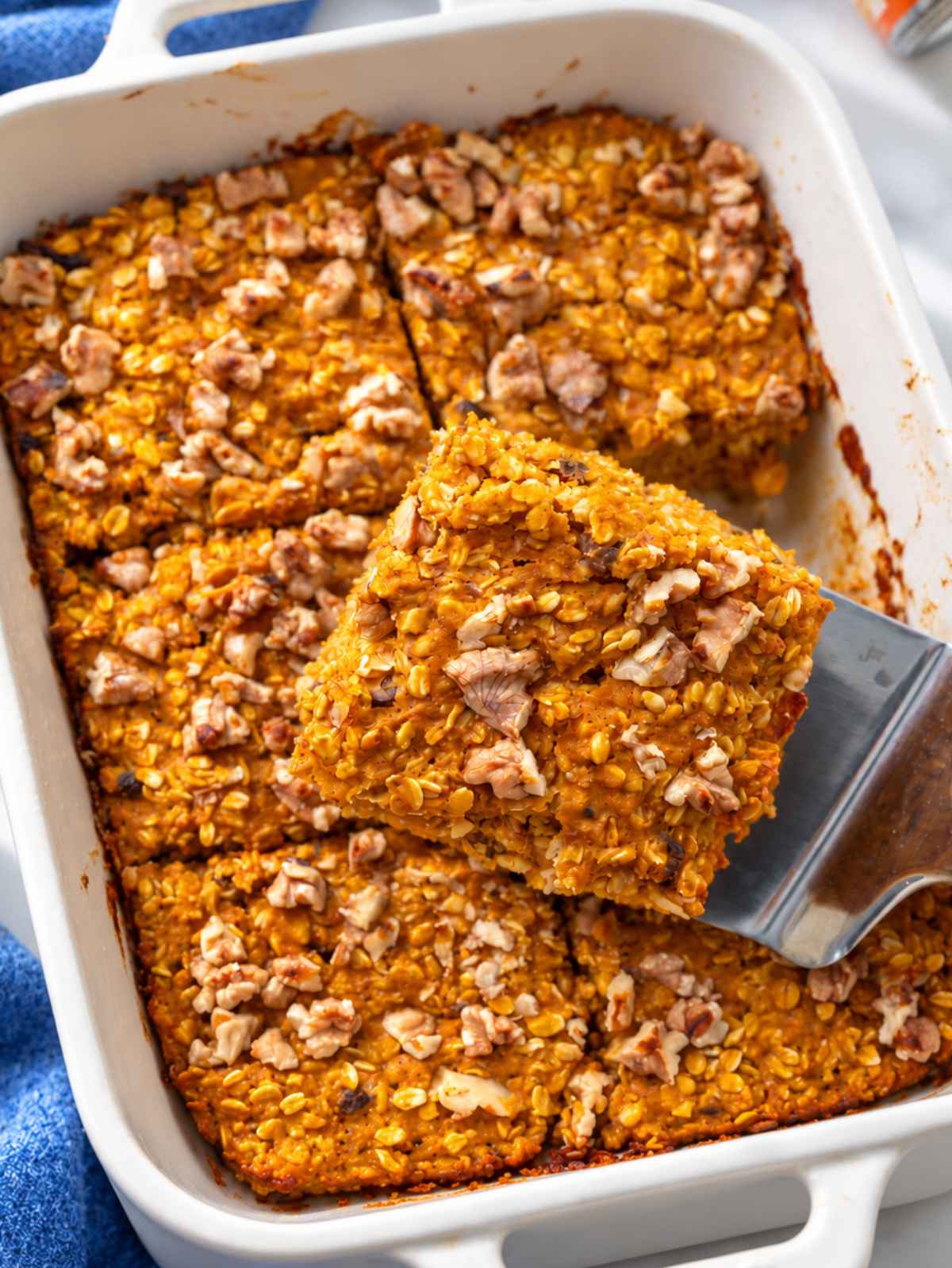 Golden pumpkin baked oatmeal squares with walnuts in a white ceramic dish.