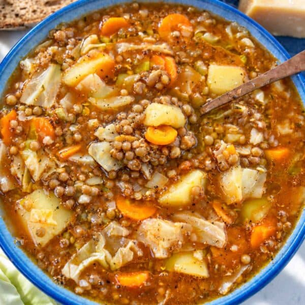 Hearty cabbage lentil soup served with crusty bread on marble.