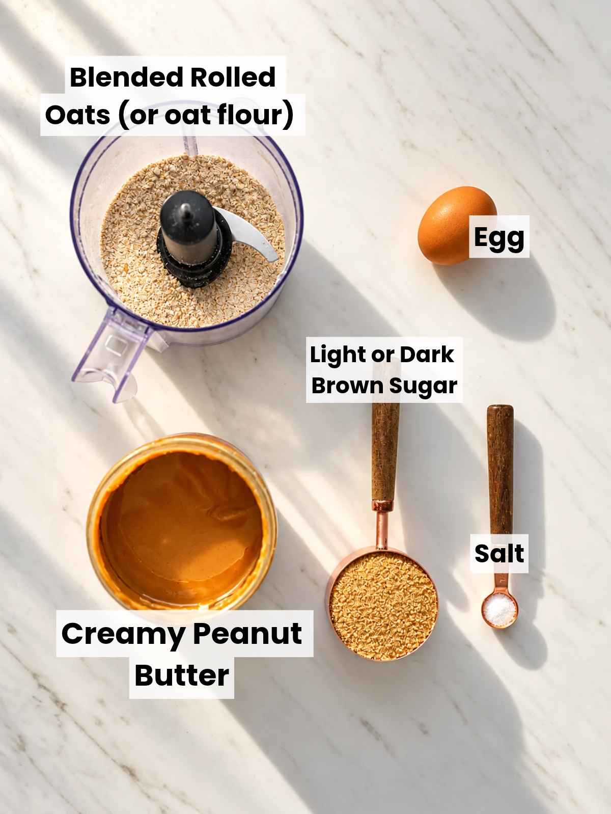 Peanut butter, brown sugar, egg, and oat flour arranged on marble.