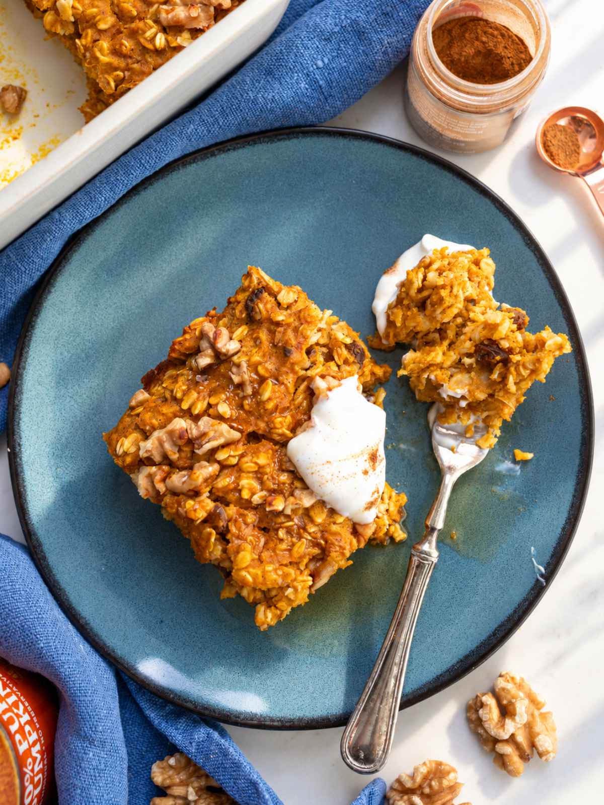 Pumpkin baked oatmeal square on a plate topped with Greek yogurt and maple syrup.