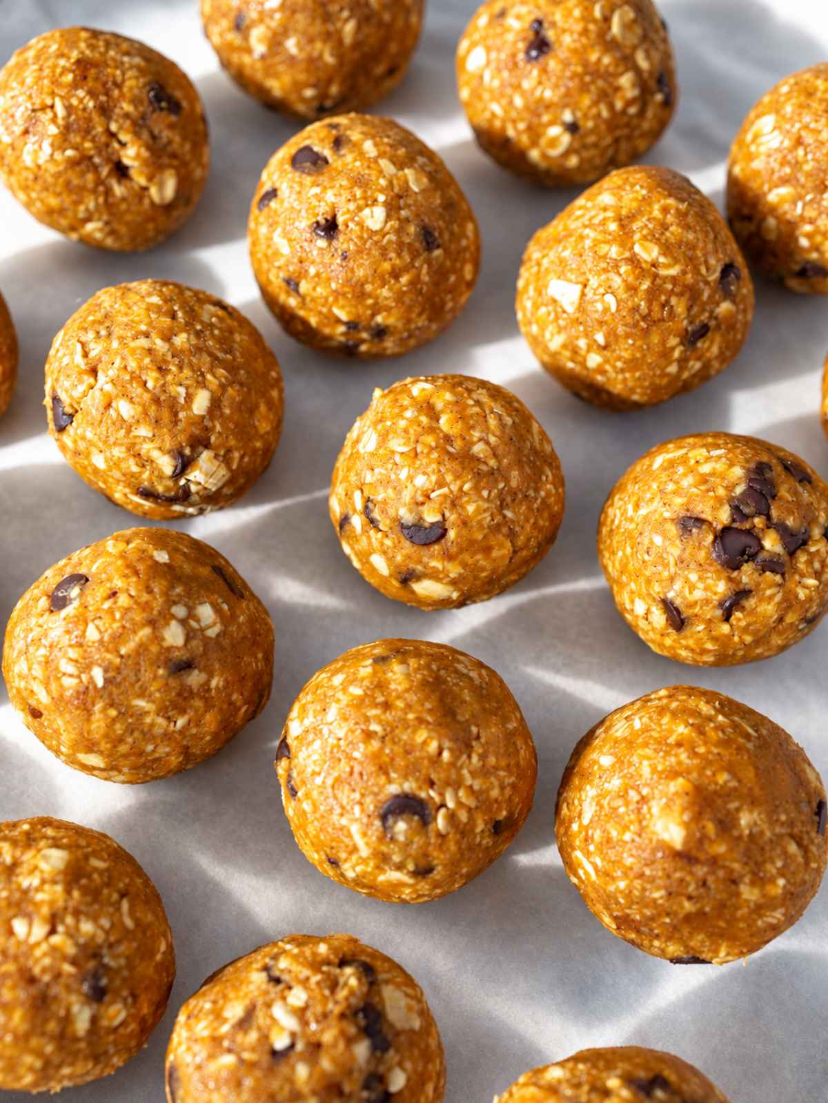 Pumpkin energy balls piled on parchment, with oats and chocolate chips visible.